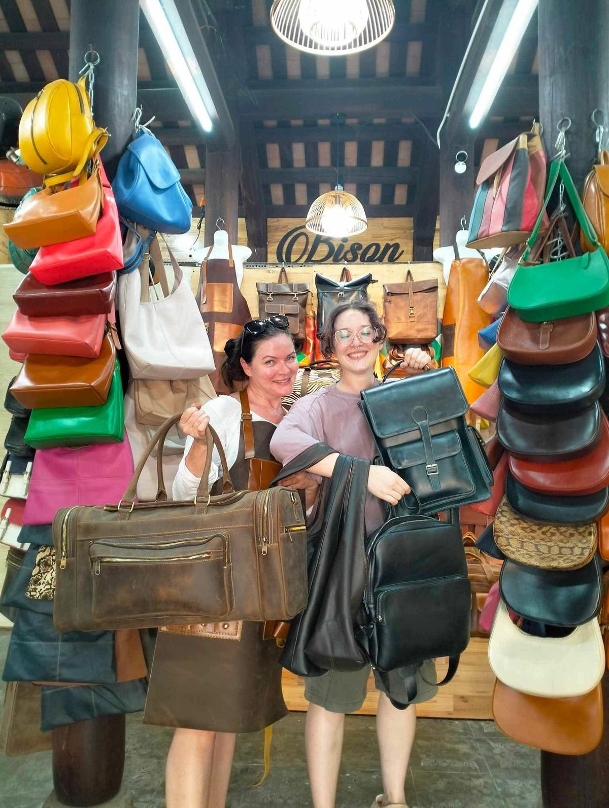 Two customers holding finished leather backpacks and a duffel from Bison Leather Shop